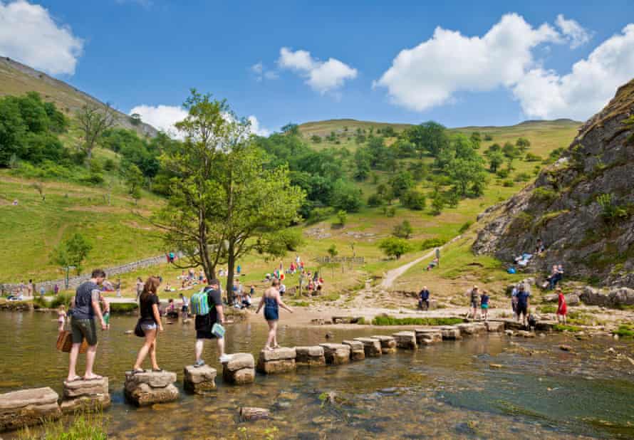 Los turistas cruzan el río Dove en Stepping Stones en el Parque Nacional Dovedale Derbyshire Peak District Inglaterra