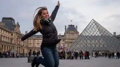 Kate jumping in the air, her knees tucked beneath her, in front of the Louvre Museum in Paris and it