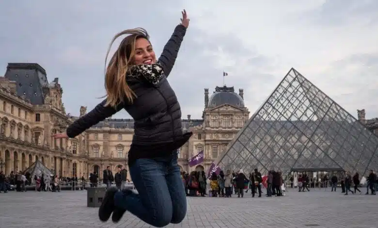 Kate jumping in the air, her knees tucked beneath her, in front of the Louvre Museum in Paris and it