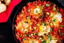 Aquí hay un primer plano de una sartén de hierro fundido con huevos turcos, tomates y pimientos, un plato típico para probar si quieres probar lo mejor de la comida turca.