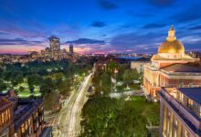Boston lit up at night, the Massachusetts State House dome glowing gold against a blue night sky and the park below.