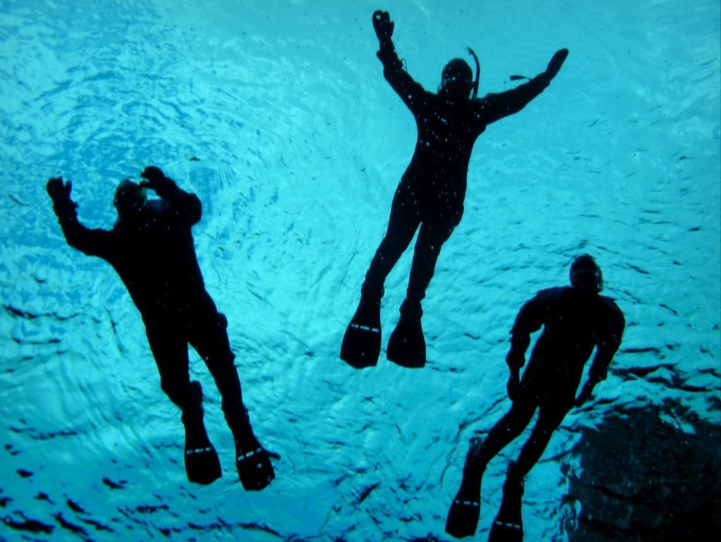 Three snorkelers in dry suits and flippers swimming in the bright blue waters of Silfra.