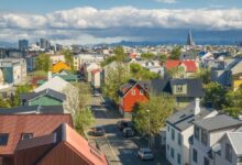 The view above Reykjavik: lots of colorful metal-sided houses with trees, the pointy church in the distance, and mountains further behind it.