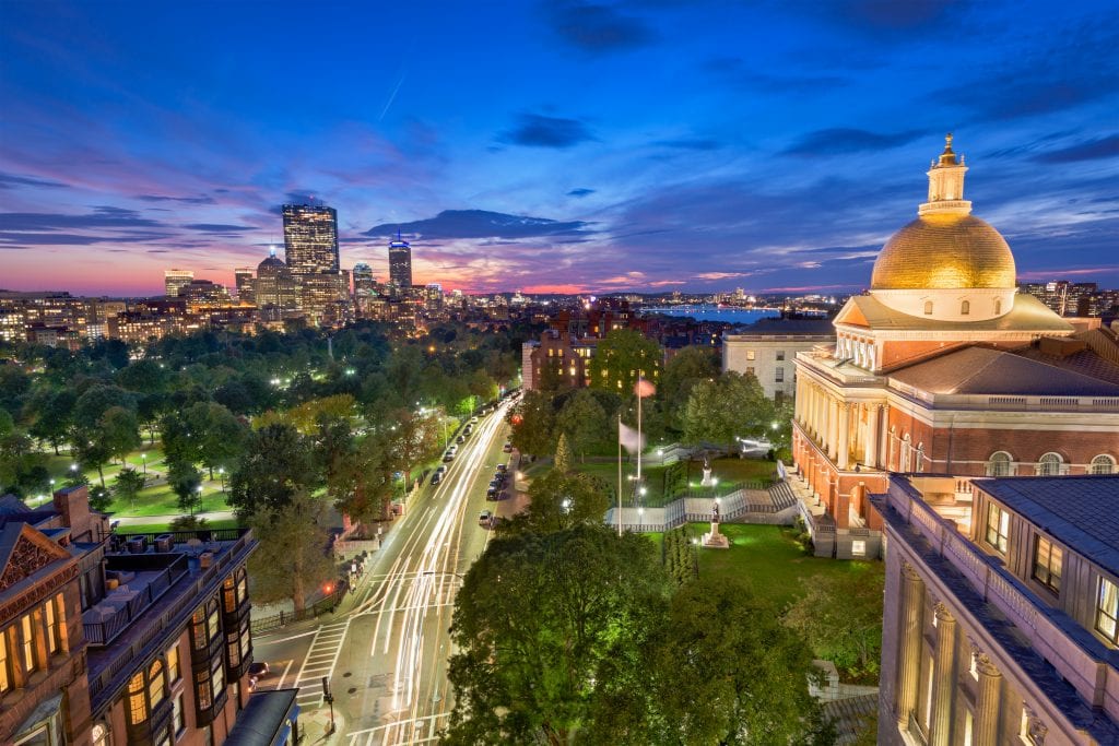 Boston lit up at night, the Massachusetts State House dome glowing gold against a blue night sky and the park below.
