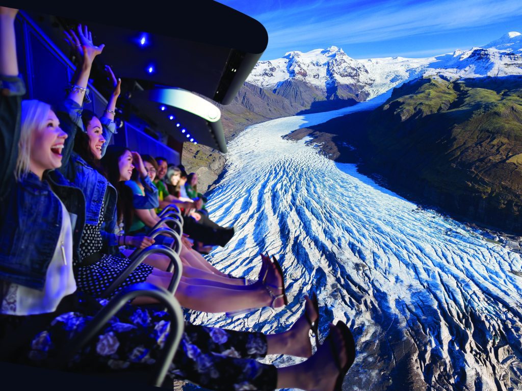People riding the FlyOver Iceland ride and enjoying the view of a glacier on screen.