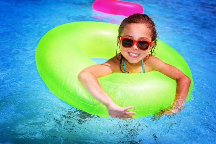 actividades familiares en Umbria |  Retrato de una linda niña feliz divirtiéndose en la piscina, flotando en agua azul refrescante con un gran anillo de goma verde, vacaciones activas de verano en la playa
