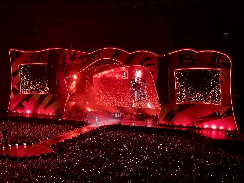 The Rolling Stones stage all lit up red, Mick Jagger standing on a catwalk in a long black suit studded with silver.