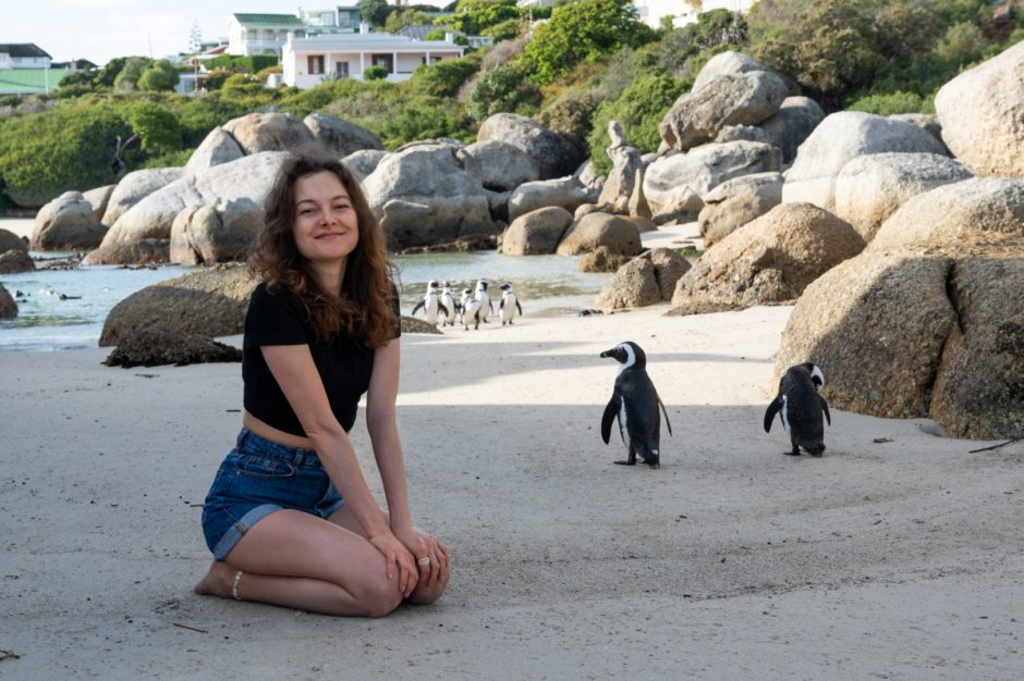 Mujer joven feliz sentada con pingüinos en la playa en Boulders