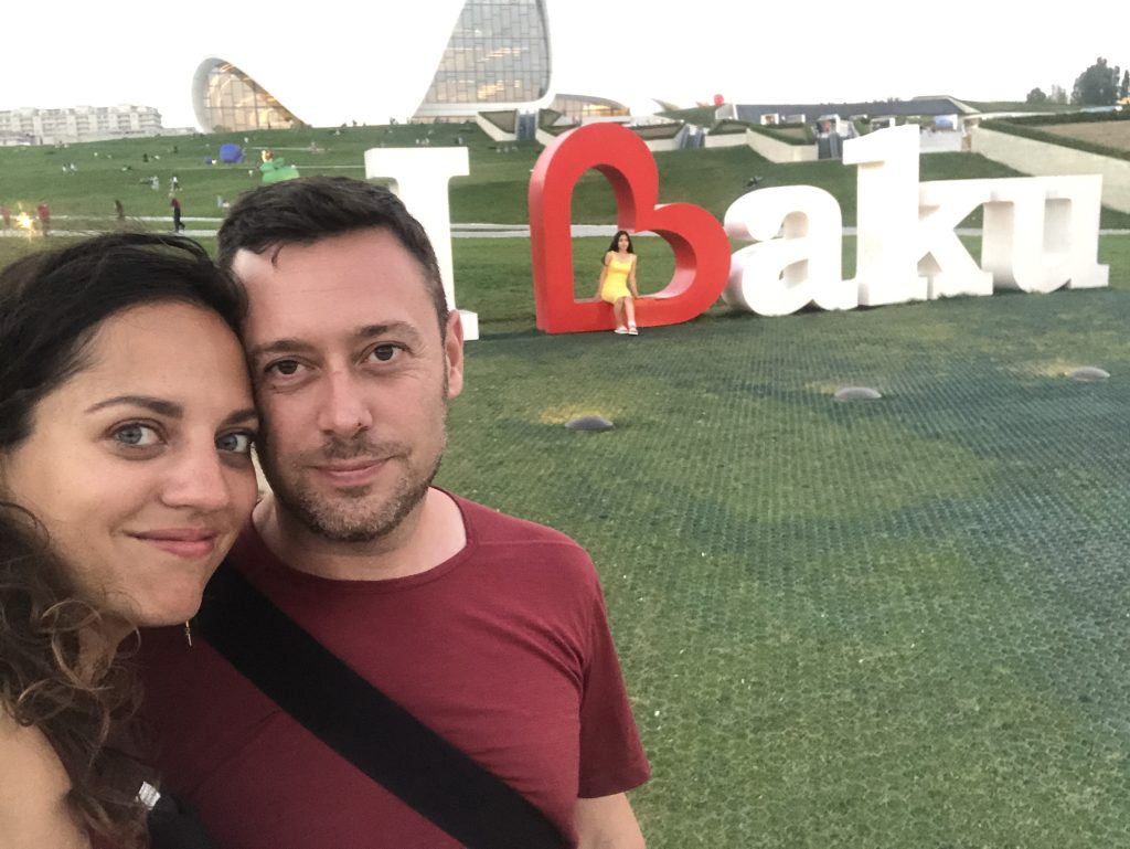 Kate y Charlie se toman una selfie sonriente frente a grandes letras sobre el césped que dicen I Baku.  La B es un corazón rojo de lado.