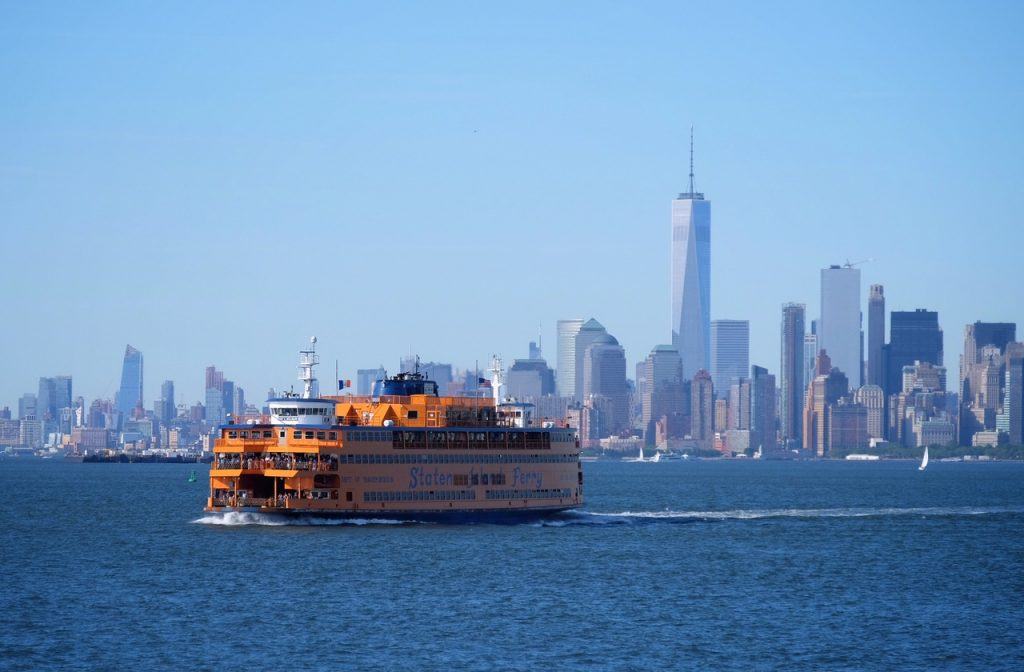 A big orange Staten Island ferry boat sailing past the Manhattan skyline.