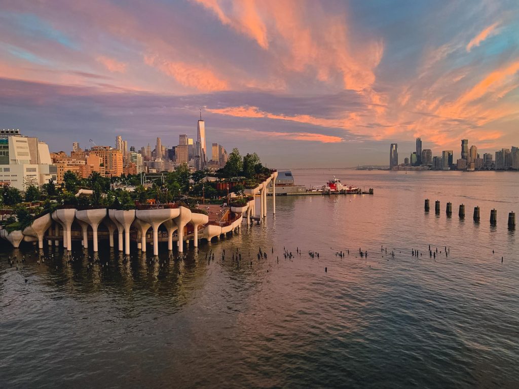 A little park on the edge of Manhattan, and lots of green space propped up on flower-like concrete planters submerged in the sea. You see the lower Manhattan skyling in the background and it's all underneath a pink sunset.