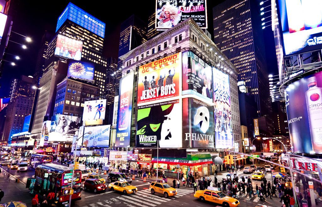 Times Square, filled with bright lights, taxis, and giant signs advertising Broadway shows like Wicked and Jersey Boys.