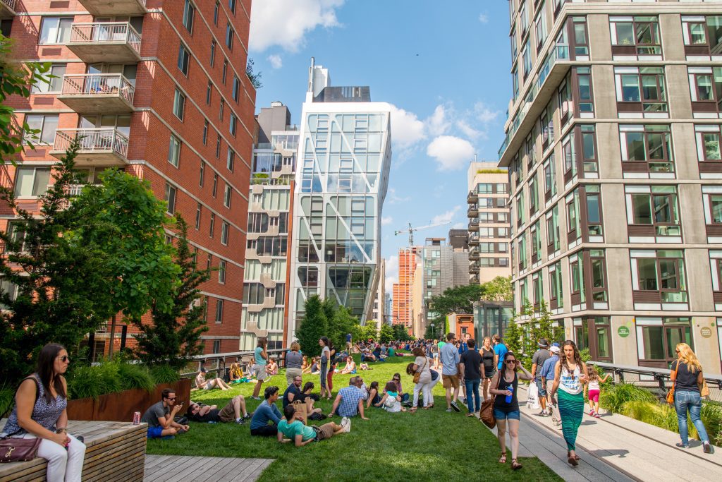 People walking and sitting in green space between two rows of buildings