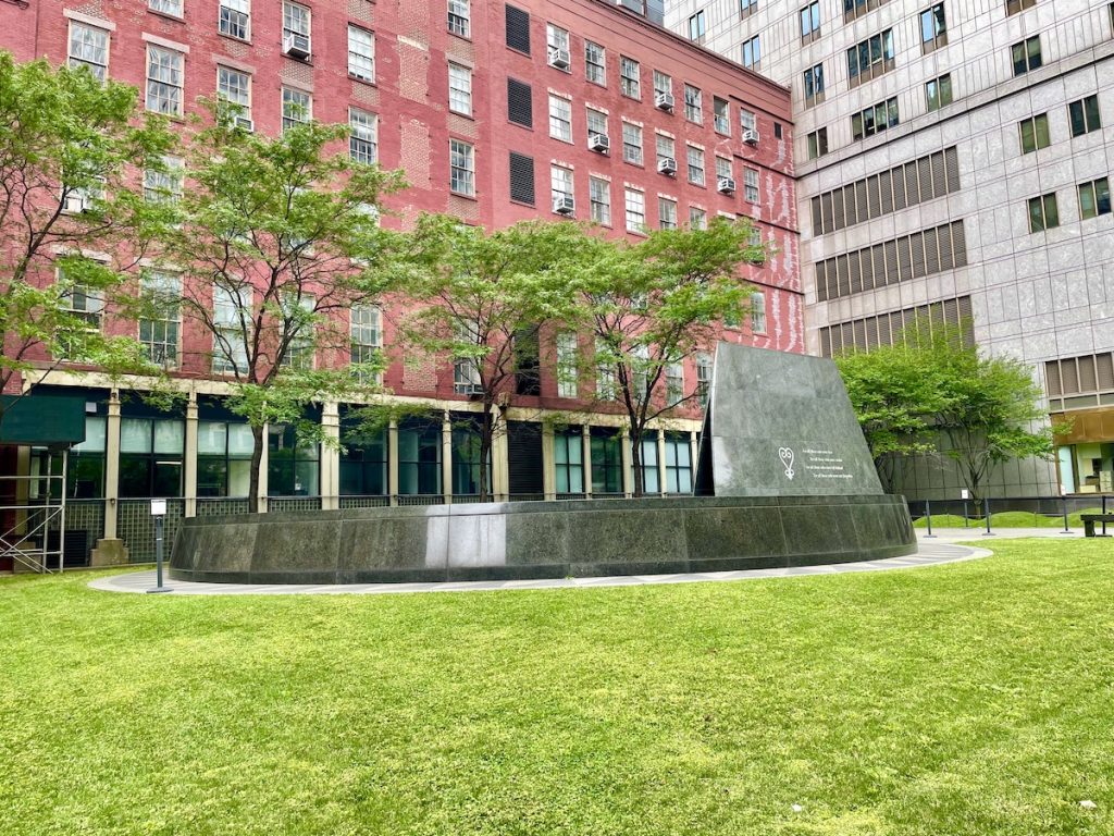 The African Burial Ground national monument with green space in front and a red building behind