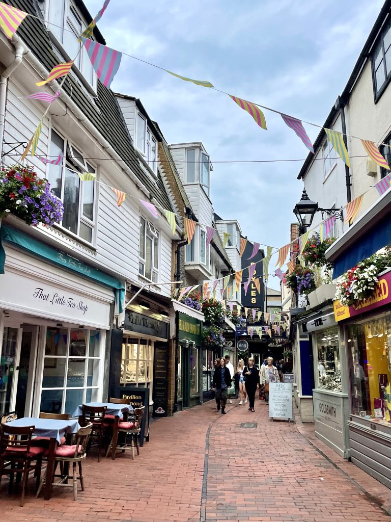 A narrow pedestrian-only street in Brighton lined with cute shops, brightly colored bunting stretched between them.