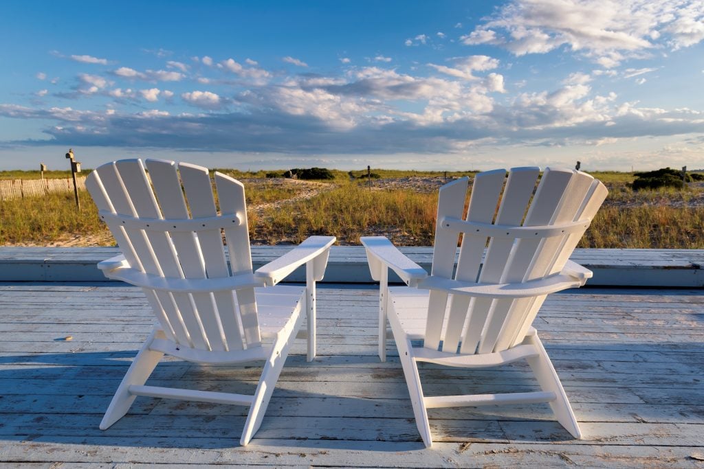 Two white chairs on a deck facing the beach in Cape Cod.
