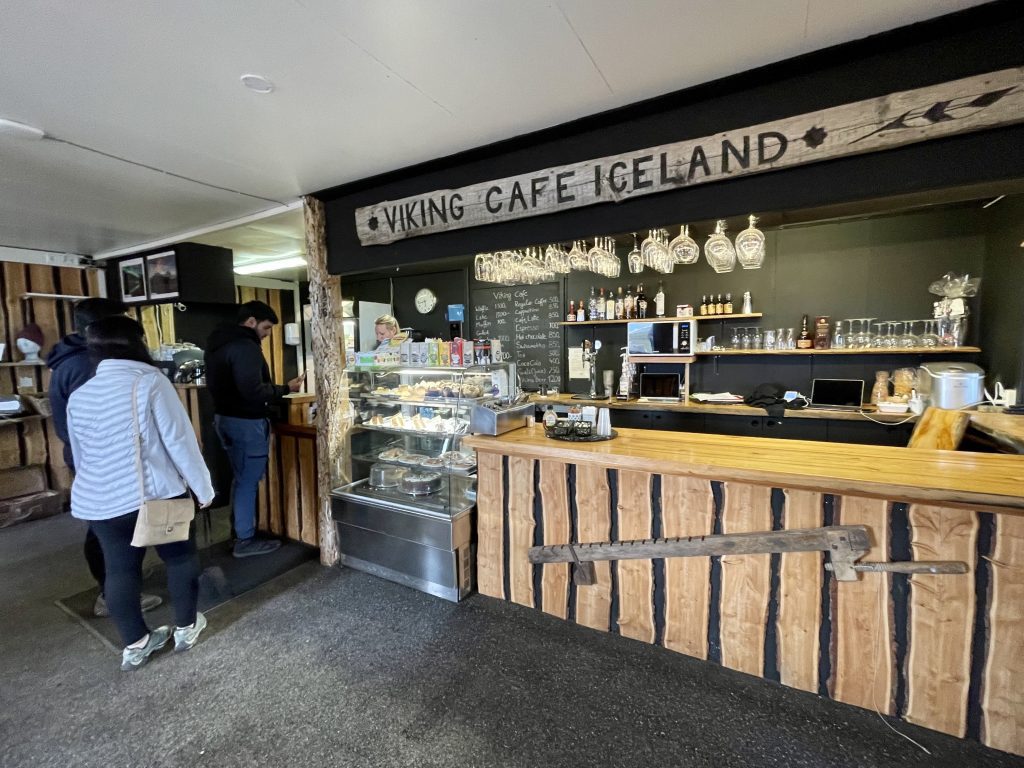 El cajero de un café con un letrero de madera en la pared que dice CAFÉ VIKINGO ISLANDIA.