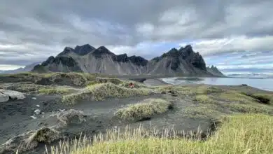 Endless hills of black sand dunes topped with green grasses, and in the background, a jagged black mountain.