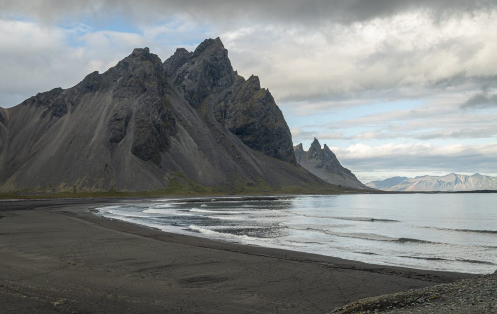 La playa negra está junto a las aguas tranquilas, con una montaña irregular negra al fondo.