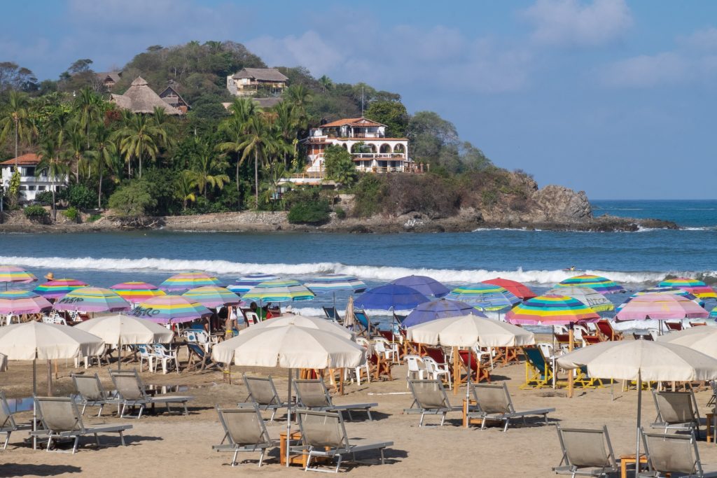 Rows of chairs with umbrellas in front of a beach with big waves.