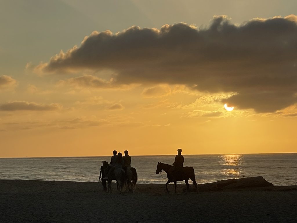 Three people riding horses on the beach at sunset.