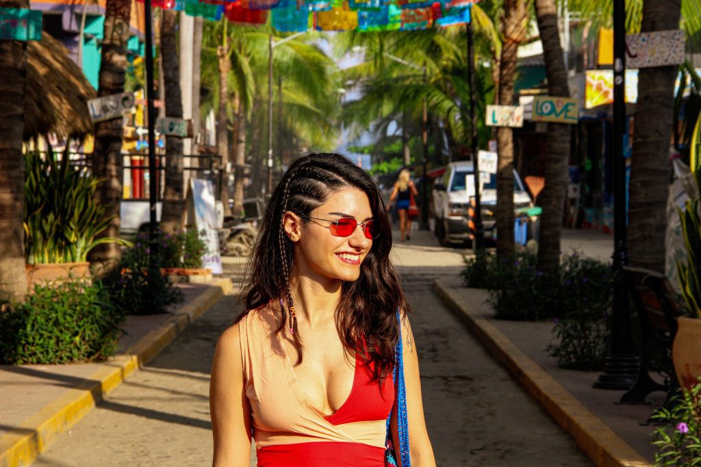 A woman in red sunglasses with braided hair walking down the flag-topped street in Sayulita