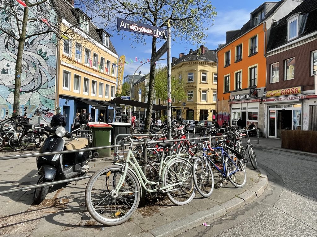 Bikes parked on a sidewalk on a blue sky day in an urban Hamburg neighborhood.