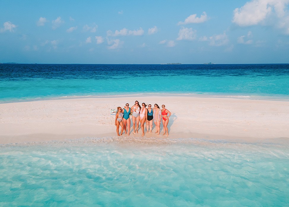 Far away shot of group of women posing on secluded beach, Maldives