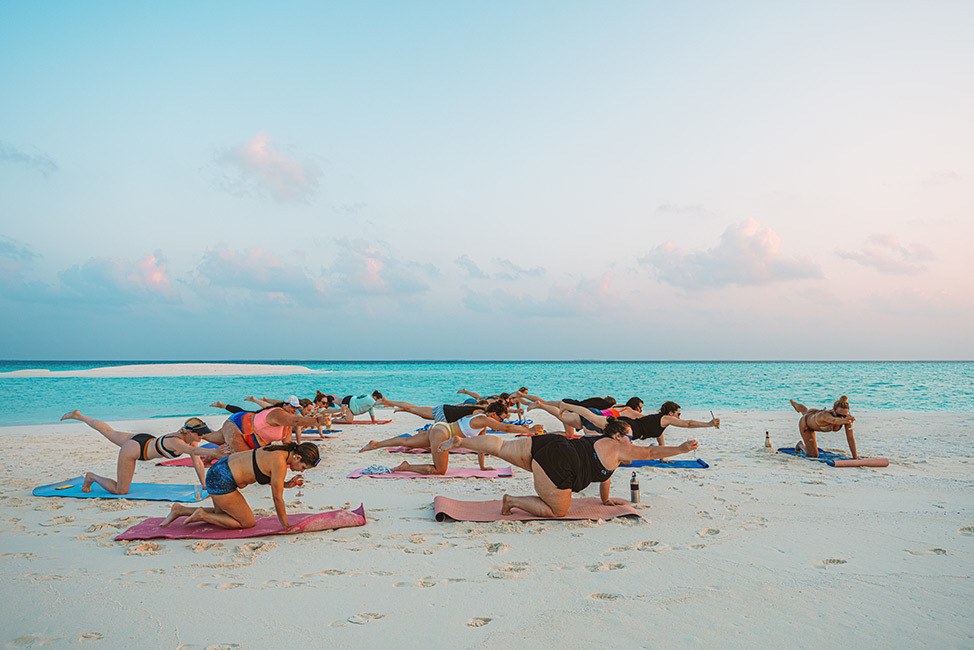 Group yoga at sunset on a secluded beach in the Maldives