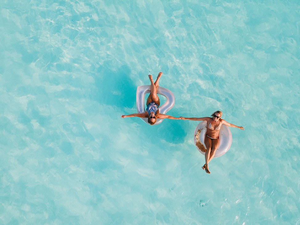 Aerial of two women floating in tubes and holding hands, Maldives