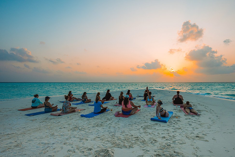 Group sitting on yoga mats facing the sunset, Maldives