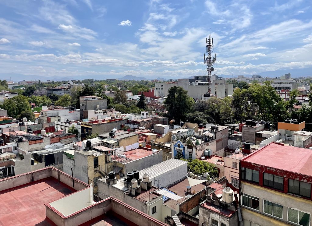 A rooftop view of Mexico City with lots of brightly colored roofs underneath a blue sky.