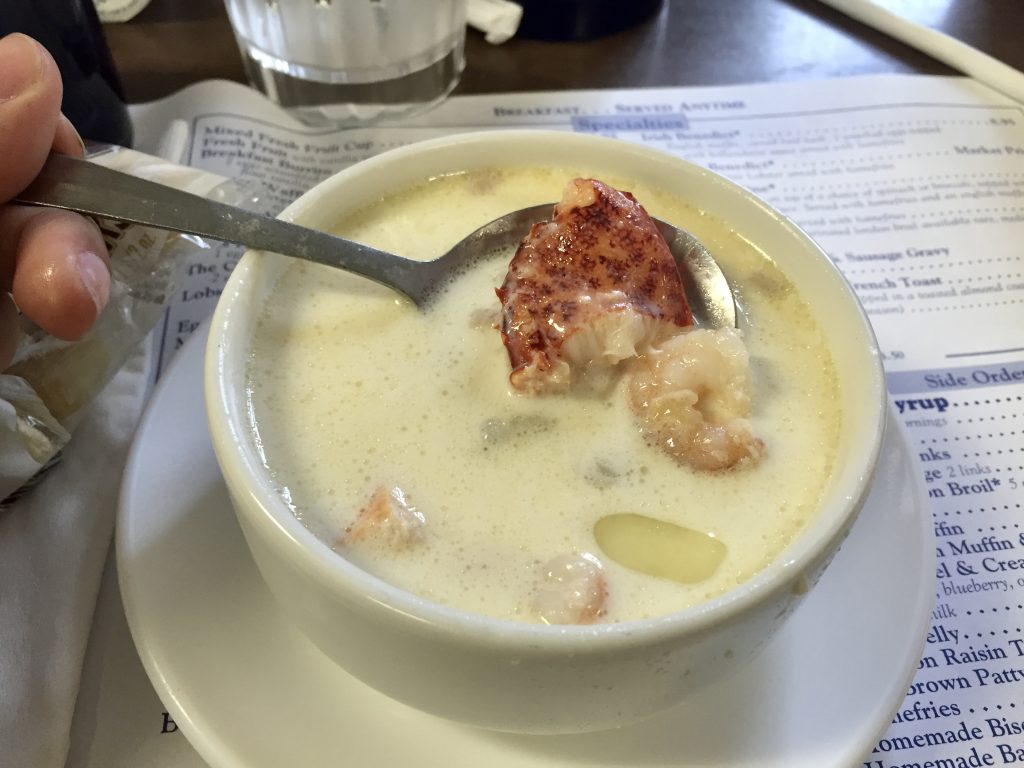 A cup of seafood chowder with a giant piece of lobster claw meat sticking out of it.
