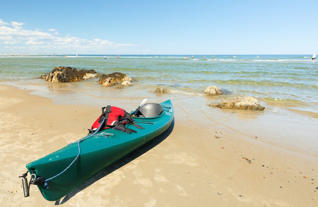 A teal kayak perched on the beach by the ocean.