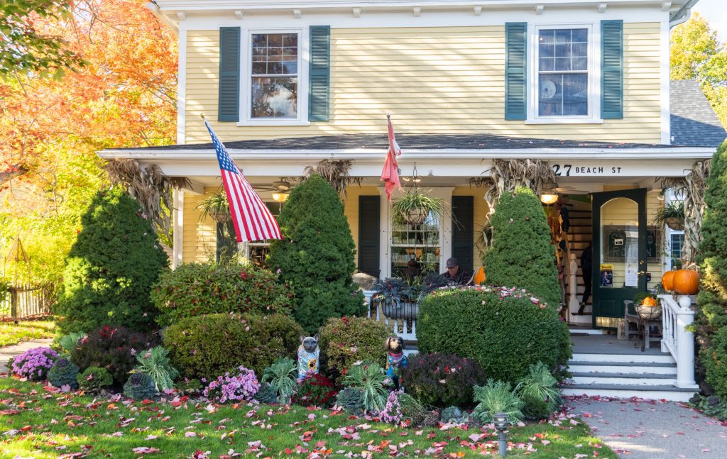 A yellow house with a front porch filled with Halloween decorations and American flags.