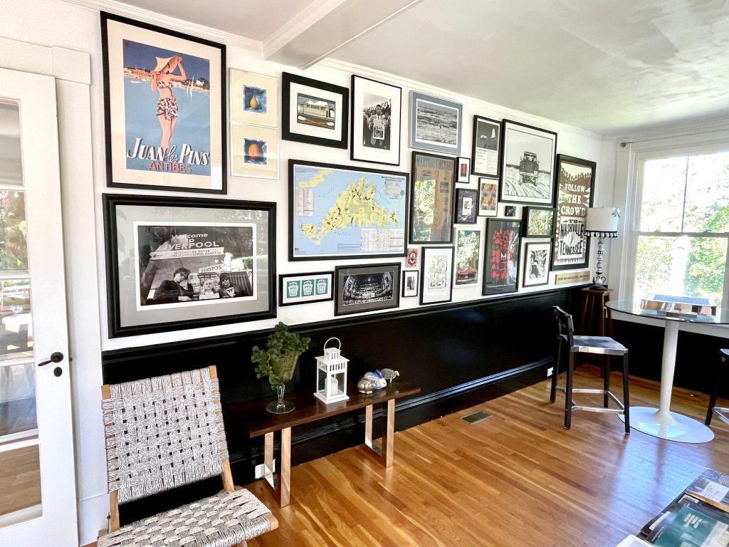 A room with a few chairs and a wall covered in framed vintage photos and maps.