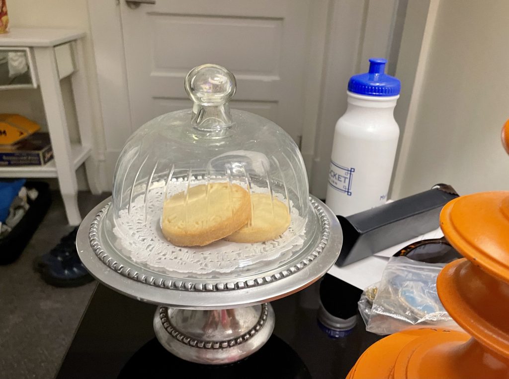 Two shortbread cookies sitting under a glass dome on a bedside table.