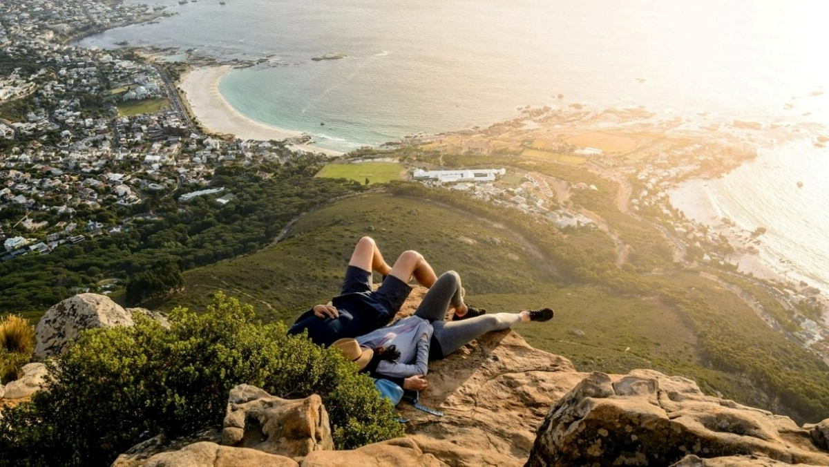 Una pareja relajándose en la ladera de una colina con vista a la playa en Ciudad del Cabo